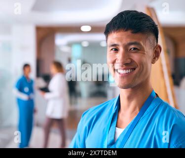 Porträt Des Lächelnden Männlichen Arztes Oder Der Krankenschwester, Der Im Krankenhaus Mit Kollegen Im Hintergrund Ist Stockfoto