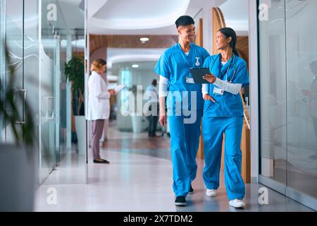 Männliche Und Weibliche Ärzte Oder Krankenschwestern In Scrubs Mit Digital Tablet Im Krankenhaus Mit Kollegen Dahinter Stockfoto