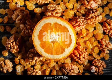 Geschnittene orange Walnüsse Rosinen auf schwarzem Holzhintergrund von oben Stockfoto