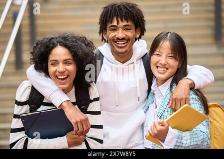 Drei junge Schüler lächeln und umarmen sich, während sie Bücher halten und in die Kamera schauen Stockfoto