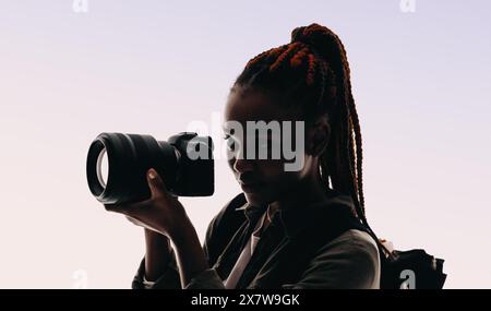 Eine junge Frau mit Rucksack und Kamera hält Momente mit einem Lächeln fest. Sie widmet sich ihrem fotografischen Hobby leidenschaftlich und macht sich auf Abenteuer. Stockfoto