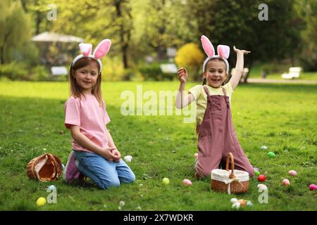 Osterfeier. Süße kleine Mädchen in Hasenohren jagen Eier draußen Stockfoto