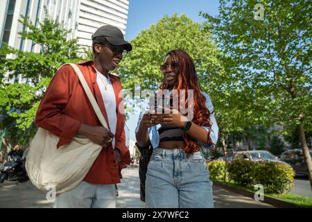 Stilvolles afroamerikanisches Paar, das draußen spricht, hört auf, auf dem Bürgersteig zu laufen, schaut auf das Bildschirm-Smartphone Stockfoto