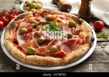 Leckere Pizza mit Räucherschinken, Oliven, Tomaten und Petersilie auf Holztisch Stockfoto