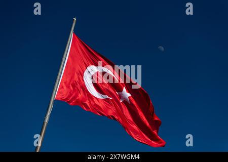 Nahaufnahme der türkischen Flagge, die vor einem klaren blauen Himmel winkt, mit dem Mond im Hintergrund. Stockfoto