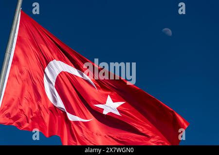 Nahaufnahme der türkischen Flagge, die vor einem klaren blauen Himmel winkt, mit dem Mond im Hintergrund. Stockfoto