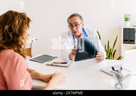 Männlicher Arzt, der mit weiblicher Patientin über medizinische Röntgenaufnahme im Krankenhaus diskutiert Stockfoto