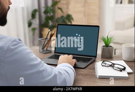 Bildschirm wird geladen, der den Fortschritt anzeigt. Mann, der drinnen am Laptop arbeitet, Nahaufnahme Stockfoto