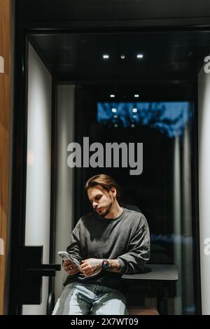 Männlicher Mann, der ein Videogespräch auf seinem Telefon in der Telefonzelle im Büro hat. Stockfoto
