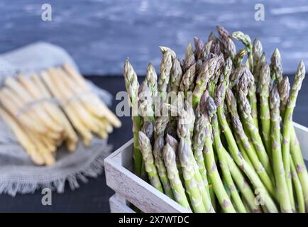 Nahaufnahme von grünem Spargel in grauer Kiste mit weißem Spargel im Hintergrund, nach der Ernte gereinigt Stockfoto