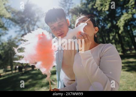 Fröhliches junges Paar, das Zuckerwatte in einem sonnigen Park genießt Stockfoto