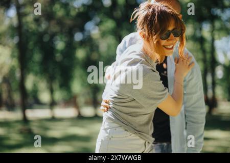 Fröhliche Frau lacht, während sie von einem Freund in einem sonnigen Park abgezogen wird Stockfoto