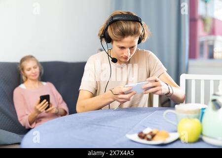 Junge, der am Telefon ein Spiel spielt, Mutter wartet auf ihn Stockfoto