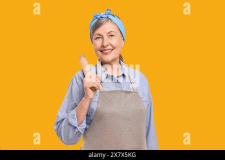 Eine glückliche Hausfrau mit einer rollenden Nadel auf orangem Hintergrund Stockfoto