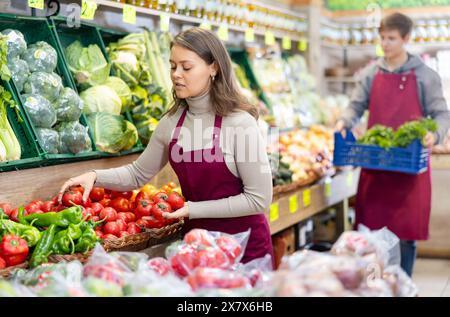 Junge Verkäuferin mit Tomaten, die auf dem Lebensmittelmarkt stehen Stockfoto
