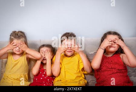 Kinder, die auf dem Sofa sitzen, bedecken ihre Augen mit ihren Händen Stockfoto