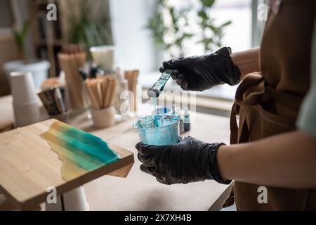 Die Künstlerin gießt Epoxidharz und schmiert es mit einem Stock auf Holzbrett, mit Hilfe von Flüssigkunsttechnik Stockfoto
