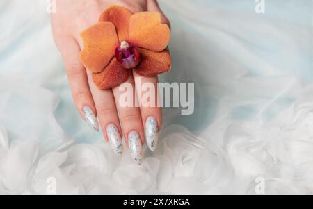 Eine Nahaufnahme zeigt eine Person Hand mit komplizierten, floralen Nailarten, die zart eine Orangenblüte umhüllt. Die umliegende weiche, schwungvolle Textur Stockfoto