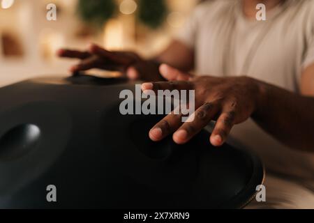 Nahhand eines nicht erkennbaren afrikanischen Mannes, der traditionelle ethnische Musik mit Glucophon spielt, der zu Hause auf dem Boden sitzt. Heitere schwarze männliche Trommeln Stockfoto