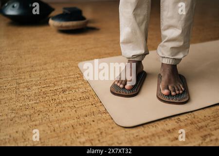 Nahaufnahme eines Afroamerikaners, der auf einem hölzernen Yoga-Sadhu-Brett mit Metallnägeln steht, um zu Hause zu üben und zu meditieren. Konzept von Stockfoto