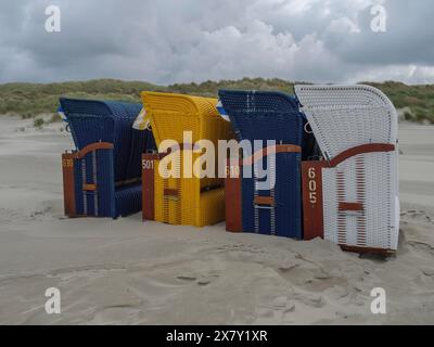 Vier bunte Liegen nebeneinander an einem Sandstrand mit bewölktem Himmel, bunte Liegen am Strand und in den Dünen mit bewölktem Himmel Stockfoto