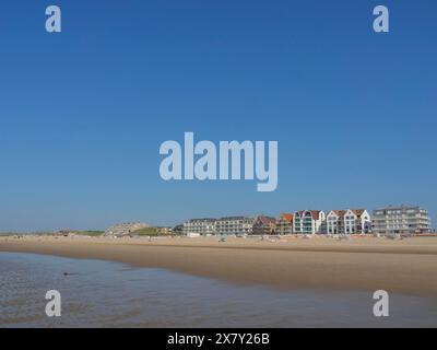 Häuser stehen an einem breiten Strand unter einem klaren blauen Himmel an der Küste, breiter Sandstrand am Meer mit Möwen und ein Stadtpanorama auf der Promenade, de h Stockfoto