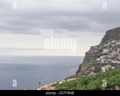 Steile Küste mit dicht besiedelten Hügeln, grünen Plantagen und Blick auf das Meer unter bewölktem Himmel, Blick auf ein kleines Fischerdorf auf den Bergen Stockfoto