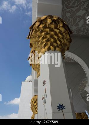 Eine verzierte Säule mit goldenen Blättern vor einem blauen Himmel, weiße Moschee mit Türmen und Kuppeln und vergoldeten Säulen, Abu Dhabi, Arabische Emirate Stockfoto