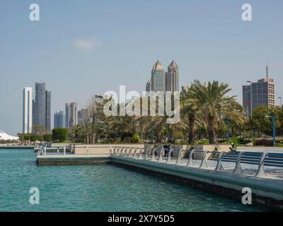 Stadtbild einer Uferpromenade mit Wolkenkratzern und Palmen im Hintergrund, von Palmen gesäumte Promenade am Meer mit Wolkenkratzern und Laternen Stockfoto