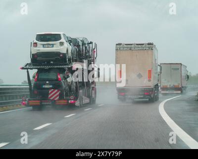 Ein Autotransporter und Lkw fahren auf einer nassen und regnerischen Autobahn unter bewölktem Himmel, regnerischer Tag auf der Autobahn A1, Piacenza, Italien, Europa Stockfoto