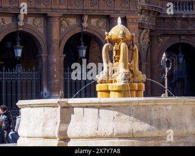 Ein Steinbrunnen mit komplizierten Skulpturen vor einem bogenförmigen, historischen Gebäude mit Menschen herum, Catania, italien, 3. Februar 2024, 3. Tag festi Stockfoto