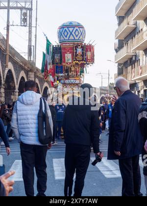 Eine Straßenprozession mit einer kunstvollen Statue, die mit Fahnen und Dekorationen verziert ist, mit einer Menschenmenge in einem städtischen Gebiet, Catania, italien, 3. Februar 2024 Stockfoto