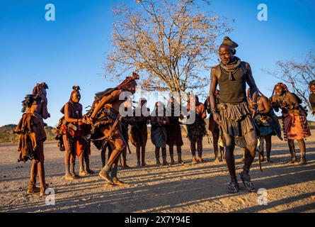 Gruppe der traditionellen Himba-Frau mit dem Häuptling des Dorfes, der in einem Halbkreis steht, klatscht und tanzt, Musik und Tanz, im Abendlicht, in der Nähe Stockfoto