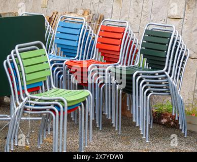 Bunte Stühle im Freien auf Kies gestapelt, mit Holzlatten in Grün, Blau, Rot und Dunkelgrün. Stockfoto