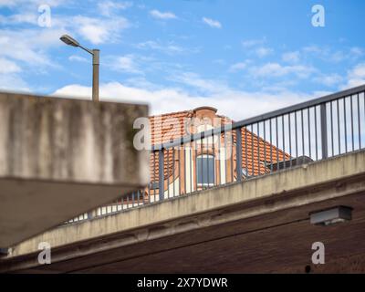 Eine urbane Szene mit einem Betonbau mit einem Geländer, einer Straßenlaterne und einem detaillierten Gebäude mit einem roten Ziegeldach. Stockfoto