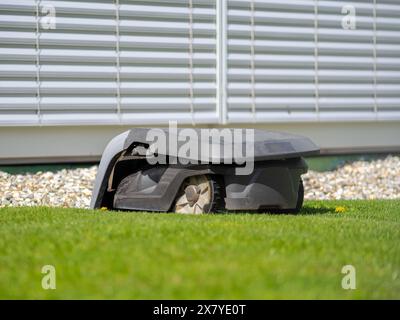 Ein moderner Mähroboter auf Gras, schlankes Design, üppig grüner Rasen, gepflegte Tagesszene. Stockfoto