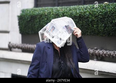 Eine Frau versteckt sich vor Regen unter einer Zeitung, während sie durch die Londoner Innenstadt geht. Starke Regenfälle könnten am Mittwoch und Donnerstag in weiten Teilen Großbritanniens zu Überschwemmungen und Reisestörungen führen, wobei für einen Teil des Landes eine gelbe Warnung ausgegeben wird. Bilddatum: Mittwoch, 22. Mai 2024. Stockfoto