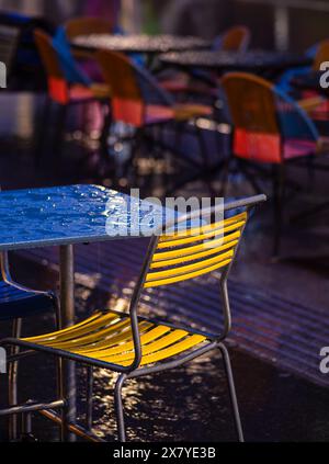 Zürich, Schweiz - 16. Mai 2024: Ein Café im Freien mit bunten Stühlen, nassen Tischen und dramatischer Beleuchtung. Stockfoto