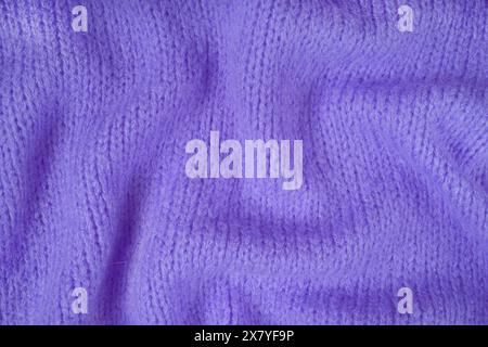 Nahaufnahme des Hintergrunds aus violettem Strickgewebe aus Viskosegarn. Zerknitterte Strickwolle, weicher Texturhintergrund. Abstrakt gestricktes Faltenmuster Stockfoto