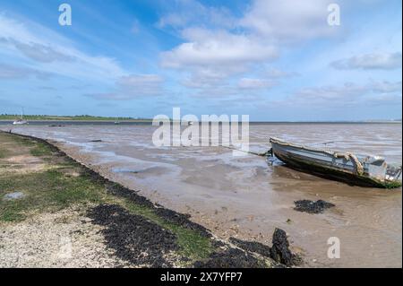 Altes graues Boot, das nahe dem Damm zur Isle of Sheppey, Kent, England im Oare Marshes Nature Reserve mit Wattflächen und einem großen Himmel vor Anker liegt Stockfoto