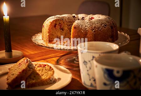 Romantisches Ambiente mit Donut, heißem Kaffee und brennender Kerze. Gemütliche Einrichtung auf Holztisch mit einem Donut und einer Tasse warmen Tee unter Kerzenlicht Stockfoto