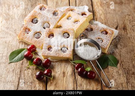 Tschechischer Bublanina Kirschkuchen mit Puderzucker-Nahaufnahme auf dem Pergament auf dem Holztisch. Horizontal Stockfoto