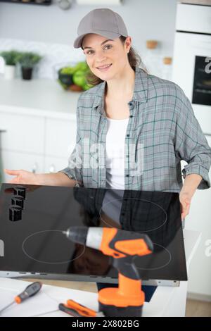 Eine Technikerin, die Kochfeld in der Küche des Kunden installiert Stockfoto