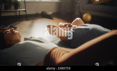 Paare mittleren Alters, die zu Hause gemeinsam im sonnigen Wohnzimmer Übungen zur Stärkung des Kerns und Crunches machen. Konzept von gesundem Lebensstil, Fitness, Erholung, Wohlbefinden und Ruhestand. Stockfoto