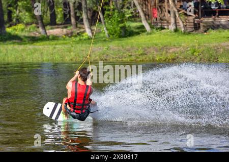 Ein Wakeboarder reitet auf einem Wasserbrett und erzeugt hinter ihm eine Sprühwolke. Stockfoto
