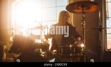 Ein ausdrucksstarkes Schlagzeugermädchen spielt Schlagzeug in einem Loft Music Proberal Studio, das mit Licht gefüllt ist. Rock Band Musikkünstler Lernt Drum Solo. Porträt einer Frau, die es genießt, Rhythmus zu kreieren. Stockfoto