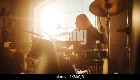 Drummer mit langen Haaren, Nasen-Piercing und starkem Make-up, in dunkler Jeans und kariertem Flanell-Shirt gekleidet, spielt Schlagzeug in einem Loft Studio Apartment. Vorbereitung auf ein Live-Konzert auf einer großen Bühne. Stockfoto