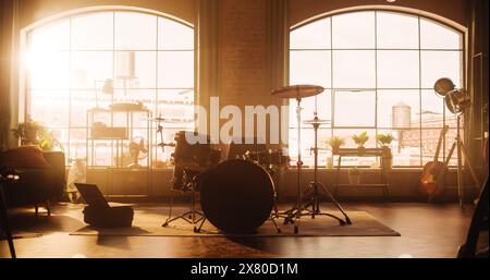 Etablierung Shot: Musikprobe Studio im Loft Room mit Drum Set in der Mitte. Stilvolles Interieur mit zwei großen Fenstern, gemütlichem Sofa, Regalen und Pflanzen. Sonniger, heller Tag und Blick auf die Stadt. Stockfoto