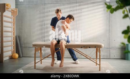 Professionelle Sportphysiotherapeutin, die mit jungen männlichen Athleten an Muskelgruppen und Rückenschmerzen arbeitet. Sportler, der sich von einer leichten Verletzung erholt. Traumaprävention Therapie oder Rehabilitation. Stockfoto