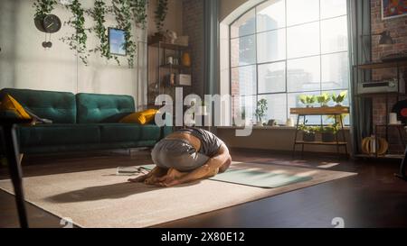 Porträt eines Happy Fit jungen Mannes, der während des morgendlichen Workouts zu Hause in der Sunny Apartment komplizierte Übungen zur Stärkung des Kerns macht. Gesunder Lebensstil, Fitness, Wohlbefinden und Achtsamkeit. Stockfoto